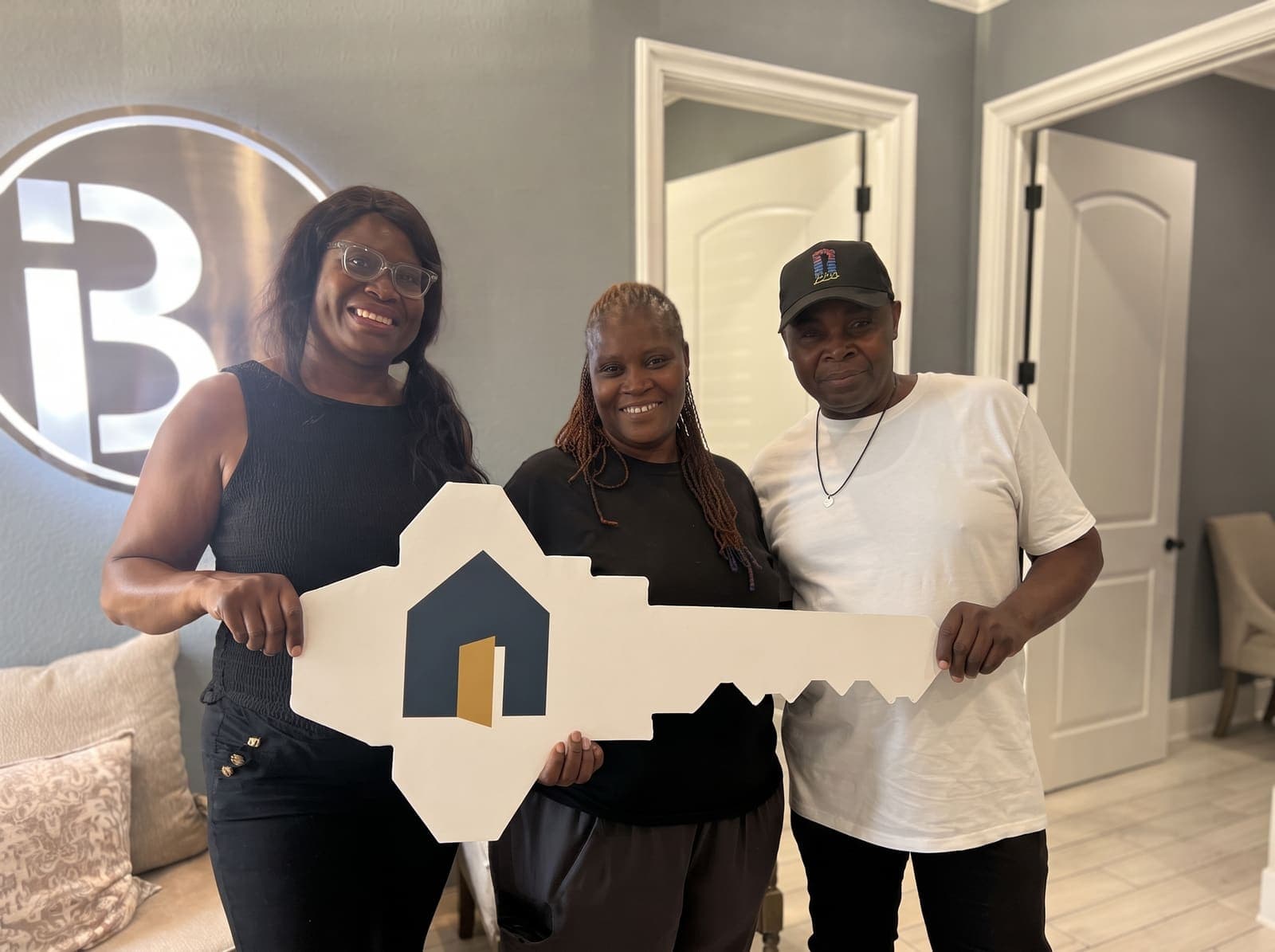 Three HomeStart members smiling together, holding an oversized house key on closing day